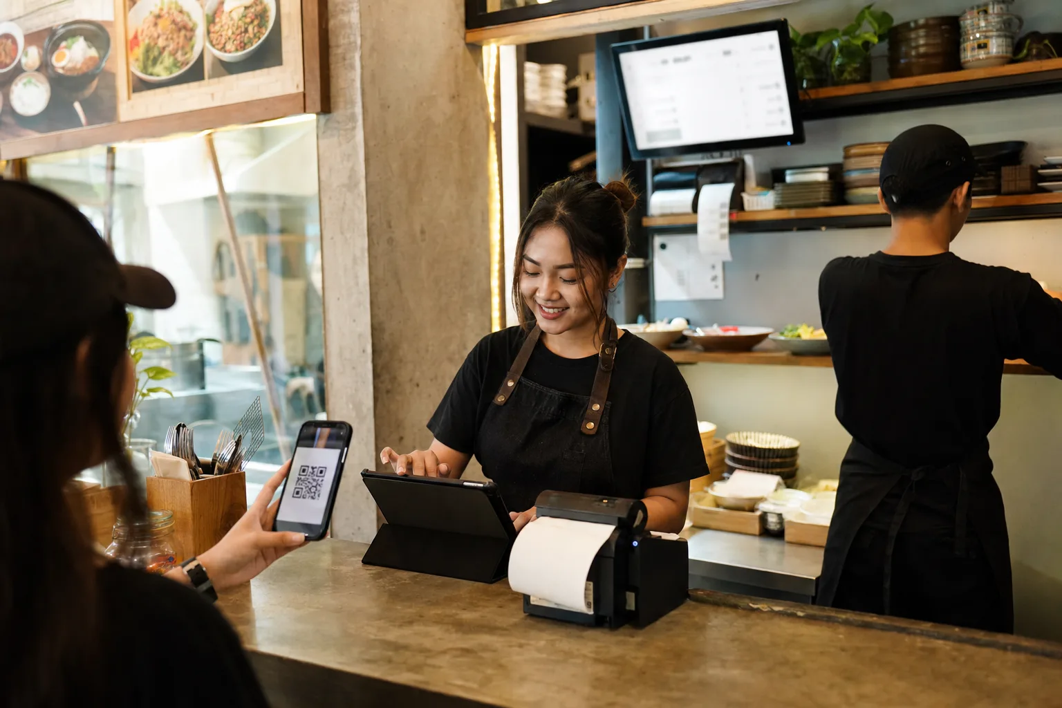 Staf kafe Indonesia memakai tablet kasir, printer struk, dan layar dapur tanpa merek